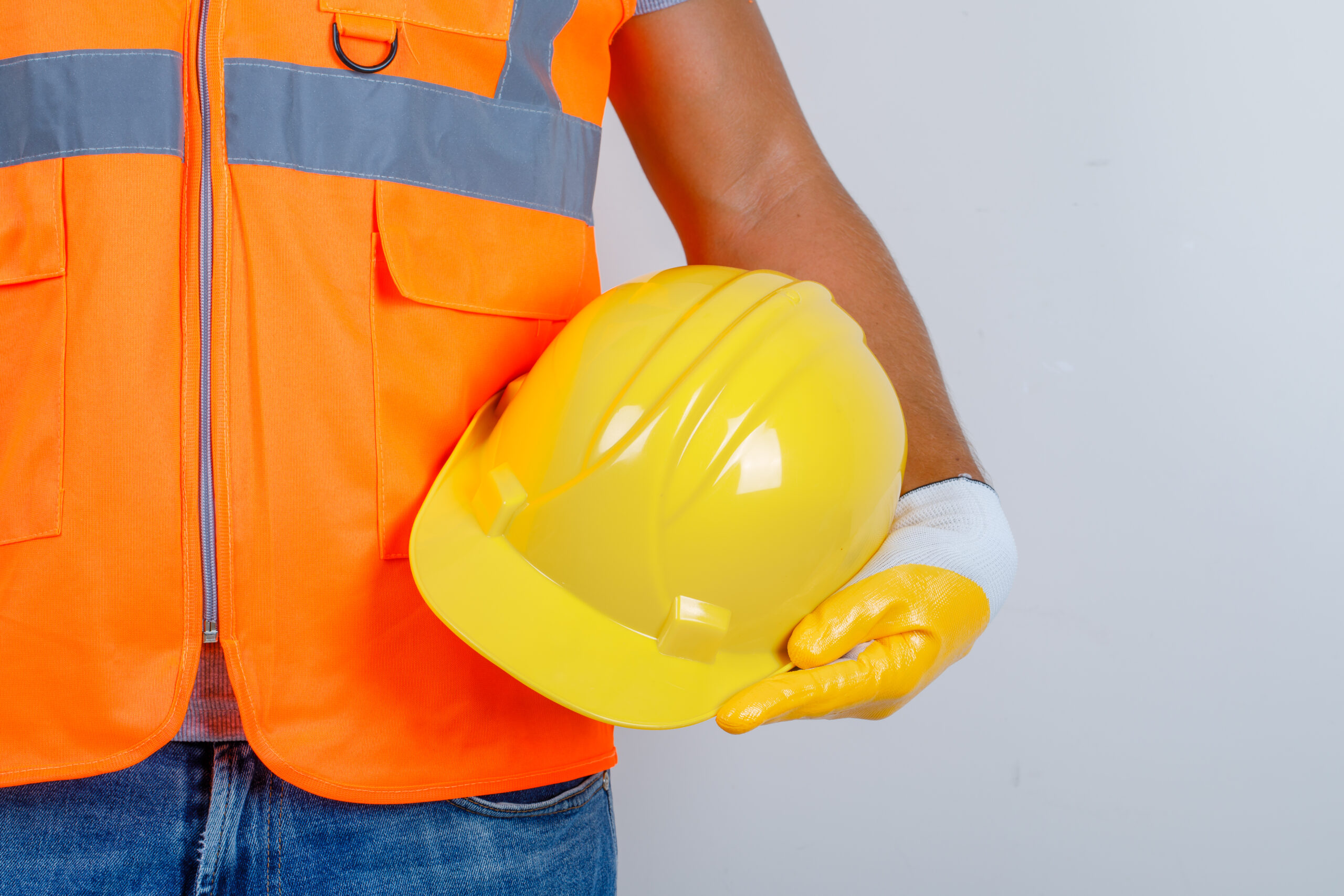 Male builder in uniform, jeans, gloves holding helmet in his hand , front view.