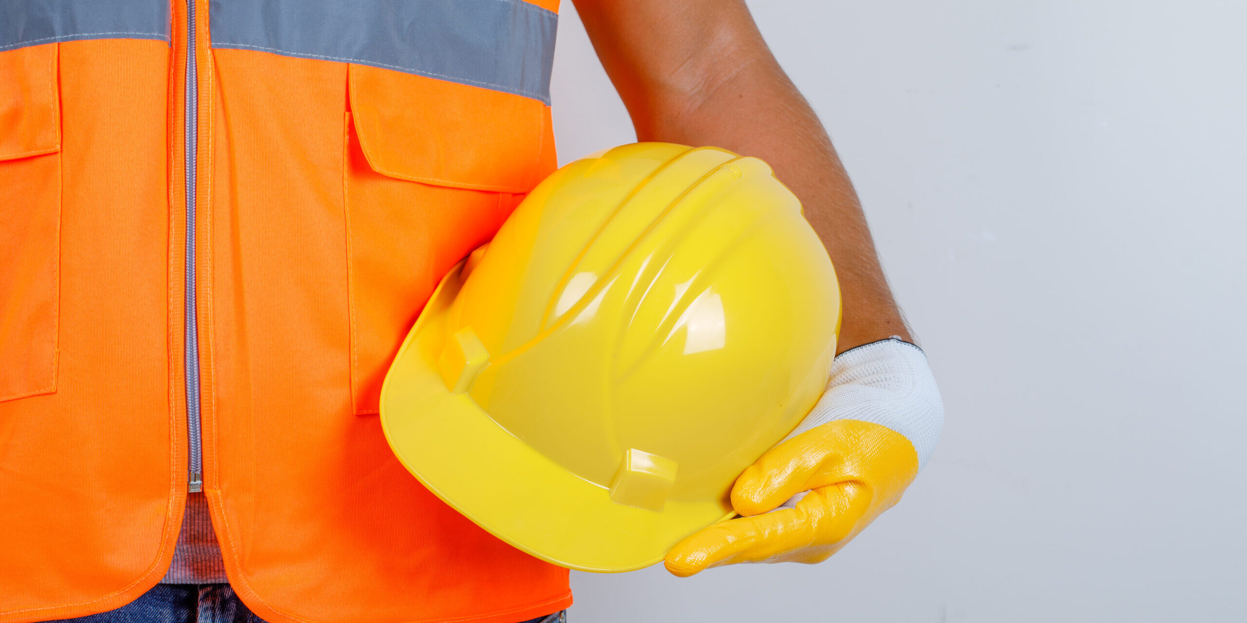 Male builder in uniform, jeans, gloves holding helmet in his hand , front view.